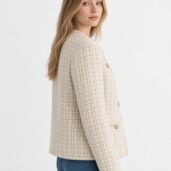 Woman in a cream plaid tweed jacket with gold buttons, viewed in profile against a light backdrop
