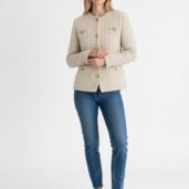 Woman modeling a beige textured button-front jacket with gold buttons, paired with blue jeans and white sneakers.