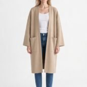 Model wearing a beige long cardigan-style coat over a white top, blue jeans, and white sneakers, standing against a plain light background