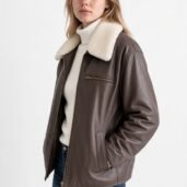 Woman wearing a brown leather jacket with a white shearling collar, white turtleneck, and blue jeans.