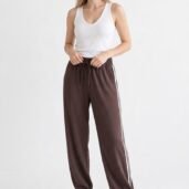 Full-body shot of a woman wearing a white sleeveless top and brown jogger pants with white side stripes, white sneakers, standing against a white background.