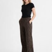 Woman standing in a black short-sleeve top and brown leopard-print wide-leg pants with hands in pockets, white sneakers