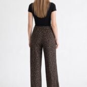 Back view of a person wearing a black short-sleeve top and brown leopard-print wide-leg pants with white sneakers.