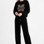 Model wearing a black velour tracksuit with a leopard‑print 'M' logo sweatshirt and matching wide‑leg pants, white sneakers, against a white backdrop.