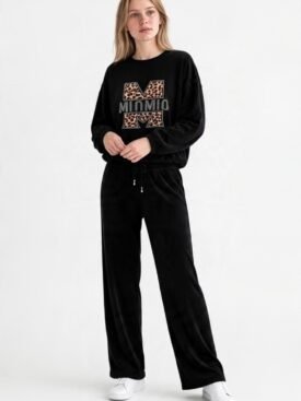 Model wearing a black velour tracksuit with a leopard‑print 'M' logo sweatshirt and matching wide‑leg pants, white sneakers, against a white backdrop.