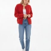 Woman in a red textured bomber jacket, white top, blue jeans, and white sneakers, standing against a white studio background.