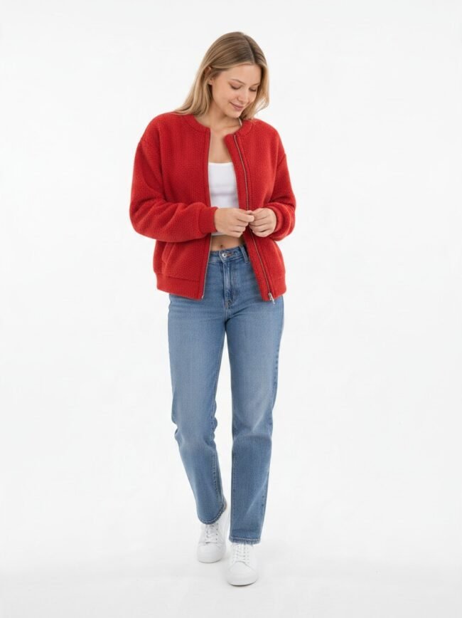 Μοντέλα μόδας AI-44c88375-b467-48e7-9072-239d3974fe24 Woman in a red textured bomber jacket, white top, blue jeans, and white sneakers, standing against a white studio background.