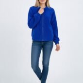 Woman in a bright blue zip-front fleece jacket, blue jeans, and white sneakers, standing against a light background.