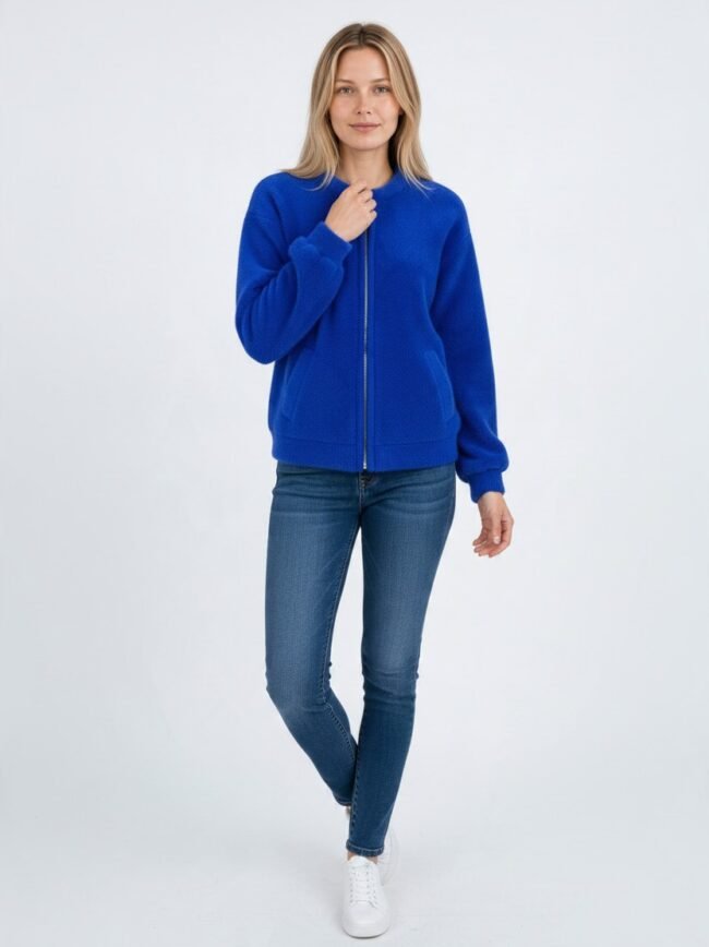 Μοντέλα μόδας AI-4808f589-8ee1-4d41-a030-38f4f61c99aa Woman in a bright blue zip-front fleece jacket, blue jeans, and white sneakers, standing against a light background.
