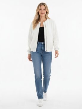 Full-body portrait of a woman in a casual outfit: white zip-front jacket, black top, blue jeans, and white sneakers in a bright studio setting.