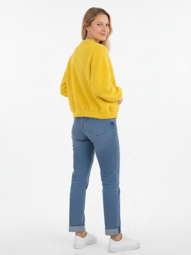 Μοντέλα μόδας AI-6ceb315f-107b-4ddc-aeba-bbae6794449d Woman in a bright yellow knit sweater, blue cuffed jeans, and white sneakers poses with her back to the camera, turning slightly to smile over her shoulder on a white backdrop.