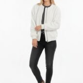 Woman in a white textured zip-front jacket over a dark top, black jeans, and white sneakers, standing against a white background.