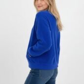 Three-quarter view of a woman in a royal blue knit sweater and jeans, with hands in pockets and a soft smile.