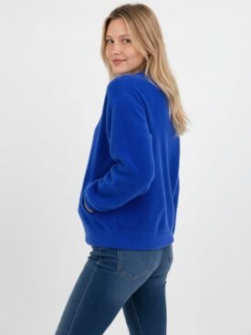 Three-quarter view of a woman in a royal blue knit sweater and jeans, with hands in pockets and a soft smile.