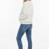 Smiling woman in a white textured sweater, blue jeans, and white sneakers, turned slightly to the side.
