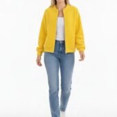 Woman modeling a bright yellow zip-front jacket over a white top, blue jeans, and white sneakers against a white background.