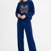 Full-body shot of a woman in a blue velour tracksuit with a leopard-print M logo and white sneakers, standing casually.