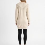 Back view of a person wearing a cream knit sweater dress with a lace chevron yoke, mid-thigh length, paired with black leggings and white sneakers.