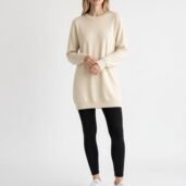 Model wearing a cream oversized sweater with black leggings and white sneakers against a plain light background.