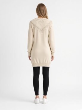 Back view of a person wearing a cream knit sweater dress with a lace chevron yoke, mid-thigh length, paired with black leggings and white sneakers.