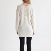 Back view of a woman in a white knit sweater with lace yoke detail and black leggings.