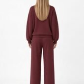 Back view of a person wearing a burgundy loungewear set: a loose hoodie with ribbed sleeves and matching wide-leg pants, long blonde hair flowing down the back.