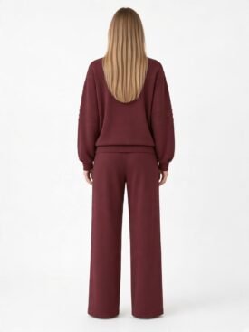 Back view of a person wearing a burgundy loungewear set: a loose hoodie with ribbed sleeves and matching wide-leg pants, long blonde hair flowing down the back.