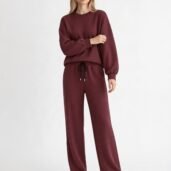 Woman in a burgundy matching sweatshirt and wide-leg joggers, white sneakers, standing against a light background with a relaxed pose to showcase the loungewear set.