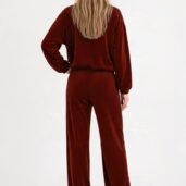 Person seen from behind wearing a burgundy velour tracksuit with a loose top and wide-leg pants, white sneakers, against a light background.