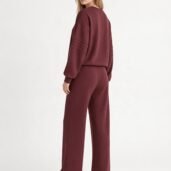 Woman in a burgundy loungewear set facing away, showcasing a matching long-sleeve top and wide-leg pants with white sneakers.