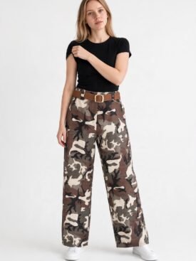 Woman in a black fitted T-shirt and wide-leg camouflage pants with a brown belt, white sneakers, standing against a light background.