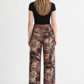 Back view of woman in a black T-shirt, brown belt, and camouflage wide-leg pants, standing against a white background.