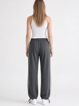 Back-view of a person wearing a white tank top and gray joggers with white side stripes, white sneakers.