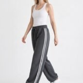Full-body shot of a woman wearing a white tank top, dark gray joggers with white side stripes, and white sneakers.