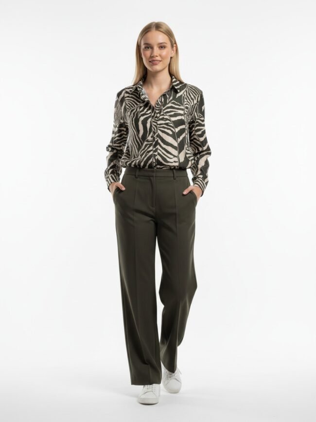 Model wearing olive wide-leg trousers and a zebra-print blouse, white sneakers, standing with hands in pockets.