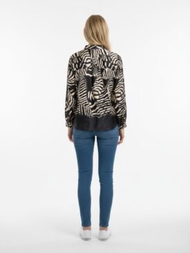 Woman seen from the back wearing a black and beige animal-print blouse, blue skinny jeans, and white sneakers in a studio setting.