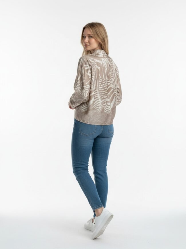 Woman standing with her back turned slightly toward the camera, wearing a beige patterned jacket, blue jeans, and white sneakers against a plain white background.