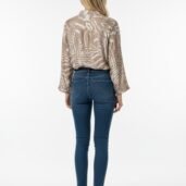 Back view of a woman wearing a beige animal-print blouse, blue skinny jeans, and white sneakers in a studio setting