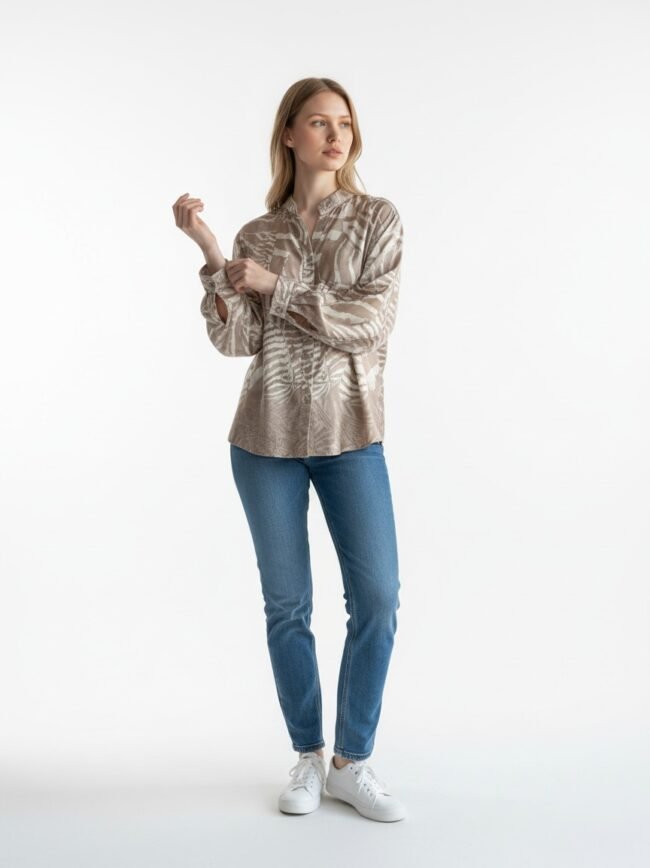 Woman wearing a beige patterned blouse, blue jeans, and white sneakers, standing against a white studio background.
