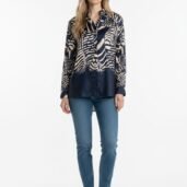 Woman standing in navy botanical-print blouse with jeans and white sneakers, facing camera with a neutral expression.