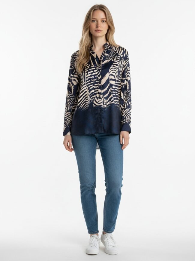 Woman standing in navy botanical-print blouse with jeans and white sneakers, facing camera with a neutral expression.