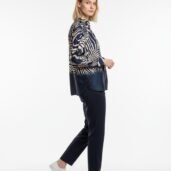 Side view of a woman wearing a navy and white zebra-print blouse, navy trousers, and white sneakers in a studio setting.
