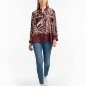 Model wearing a burgundy abstract-print blouse with blue jeans and white sneakers against a white background.
