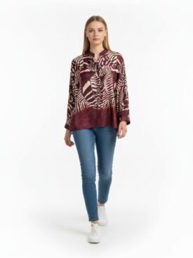 Model wearing a burgundy abstract-print blouse with blue jeans and white sneakers against a white background.