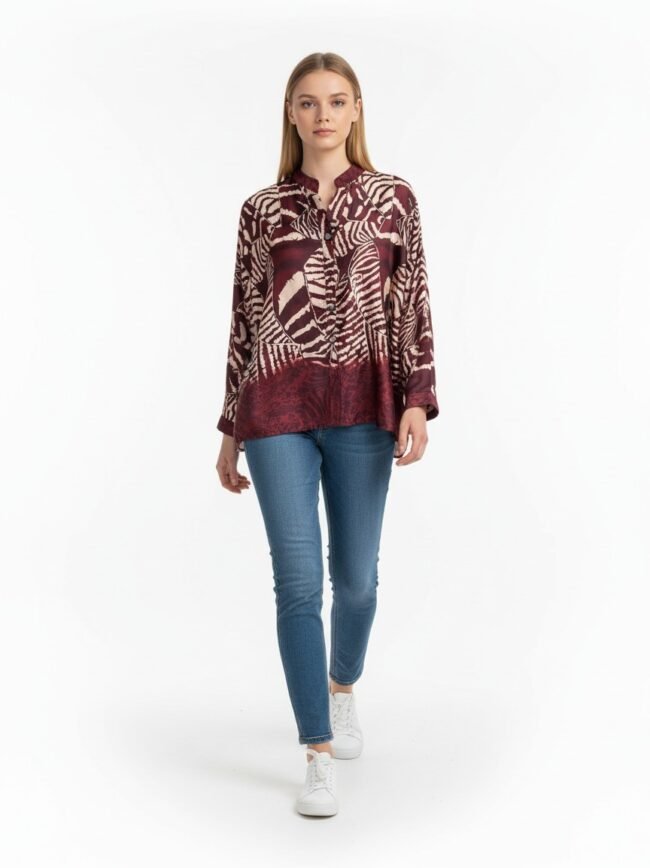 Model wearing a burgundy abstract-print blouse with blue jeans and white sneakers against a white background.