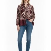 Full-body shot of a woman wearing a burgundy patterned blouse, blue jeans, and white sneakers against a white background.
