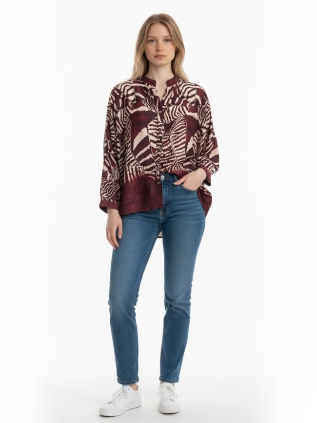 Full-body shot of a woman wearing a burgundy patterned blouse, blue jeans, and white sneakers against a white background.
