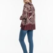 Side view of a woman in a burgundy zebra‑print coat over blue jeans and white sneakers, standing against a white background.
