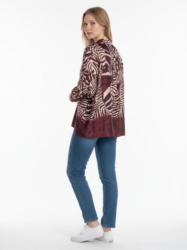 Side view of a woman in a burgundy zebra‑print coat over blue jeans and white sneakers, standing against a white background.