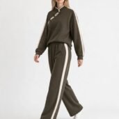 Model wearing an olive-green tracksuit with white side stripes and white sneakers, walking forward.